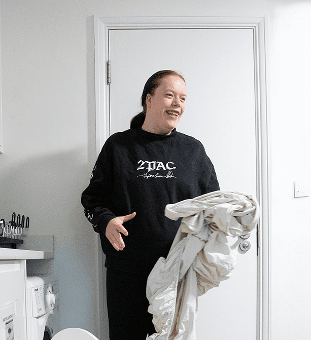 Service user standing next to a washing machine, actively engaged in doing laundry.